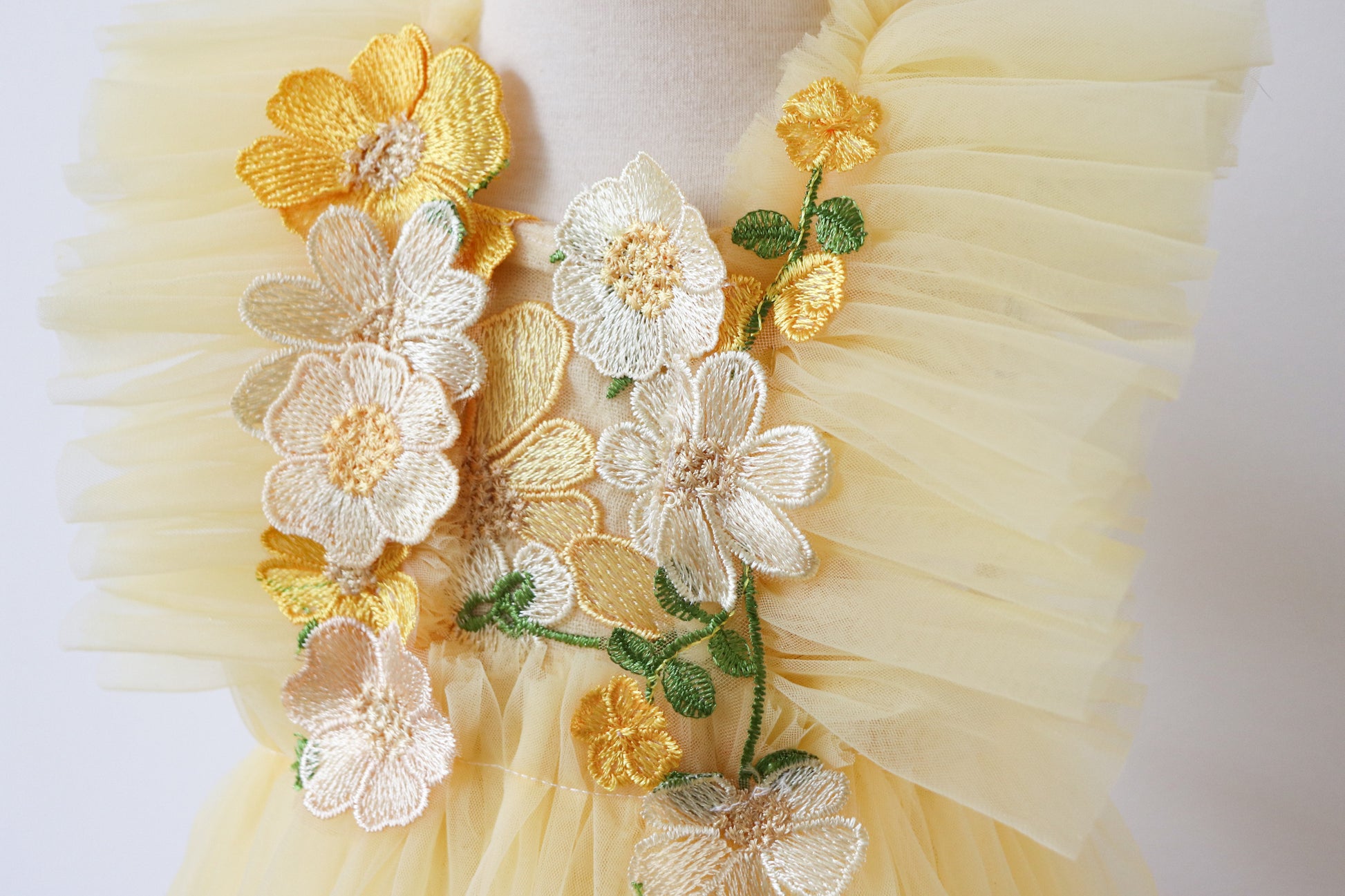 Close-up of a charming yellow playsuit for girls, featuring embroidered flowers on the bodice, soft tulle ruffles, and a classic overall silhouette, perfect for springtime adventures
