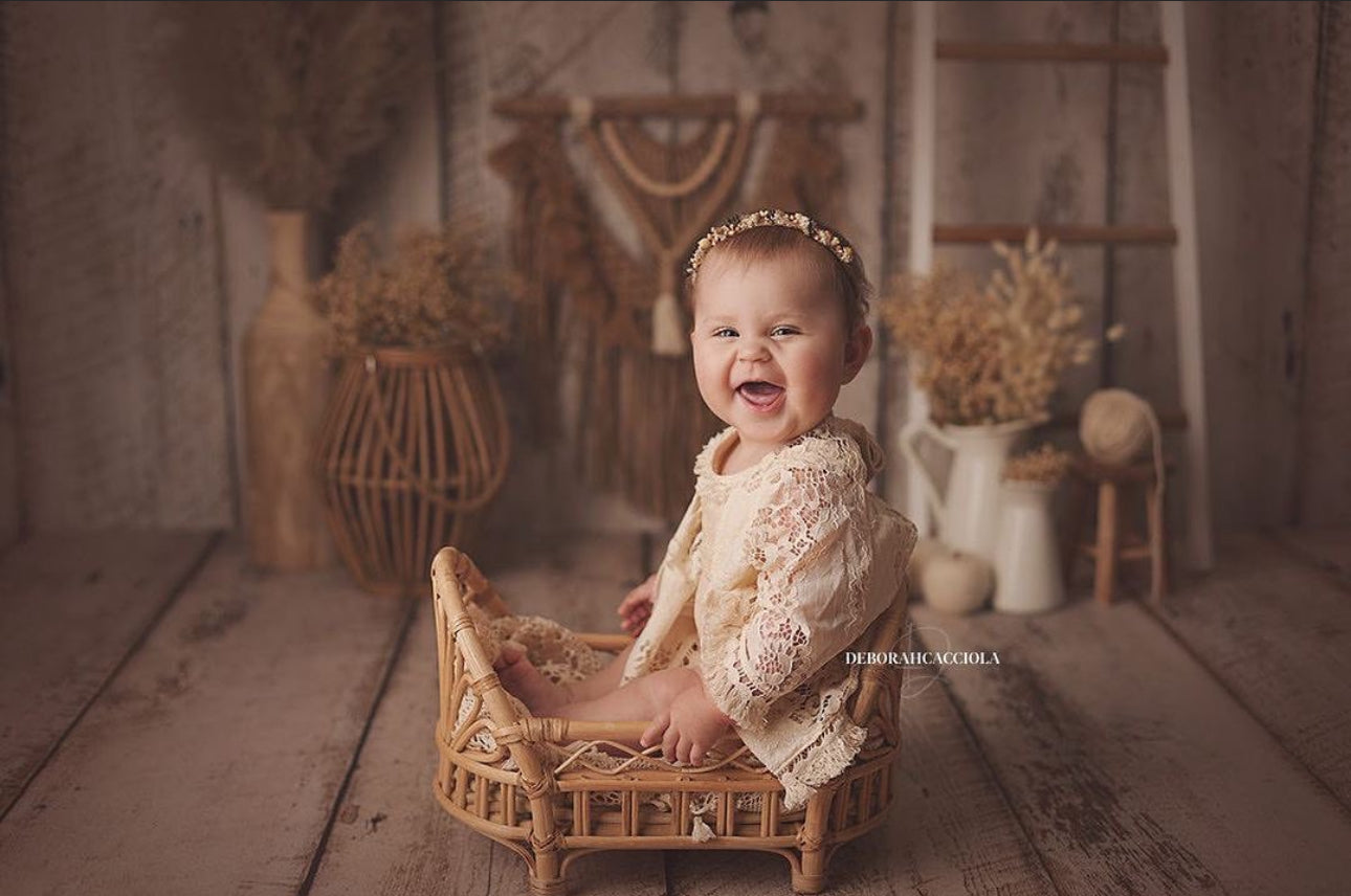 Smiling baby girl in lace boho girl photoshoot outfit sitting on small wicker chair indoors