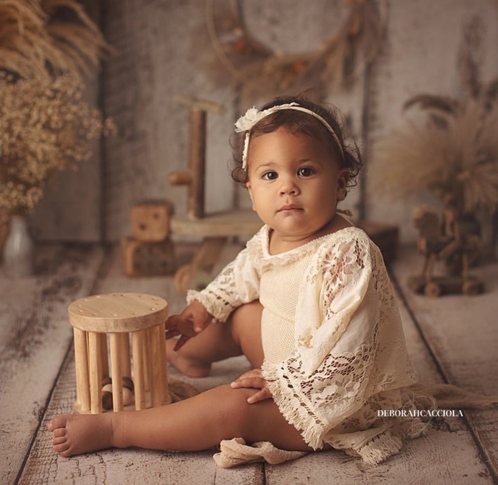 Boho girl photoshoot outfit featuring a baby girl in a cream lace dress and headband sitting on rustic wooden floor