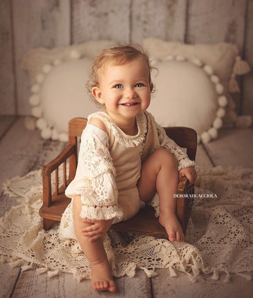 Smiling baby girl in boho girl photoshoot outfit sitting on wooden chair with crochet blanket