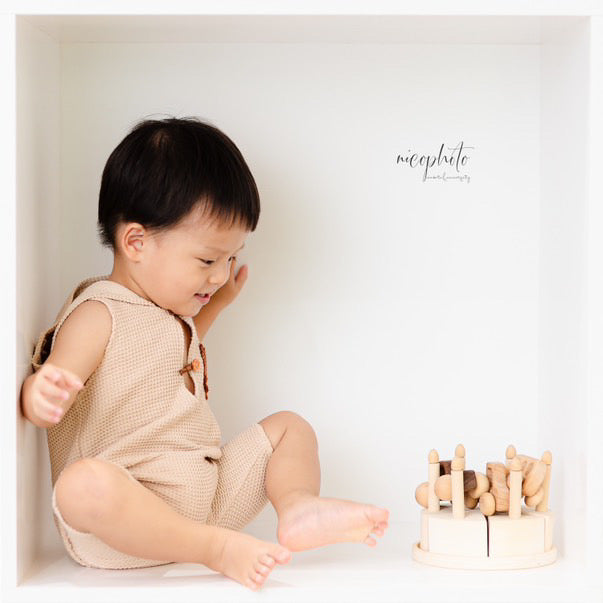 Baby boy wearing a beige sitter romper for photoshoot sitting inside a white cube with wooden toys
