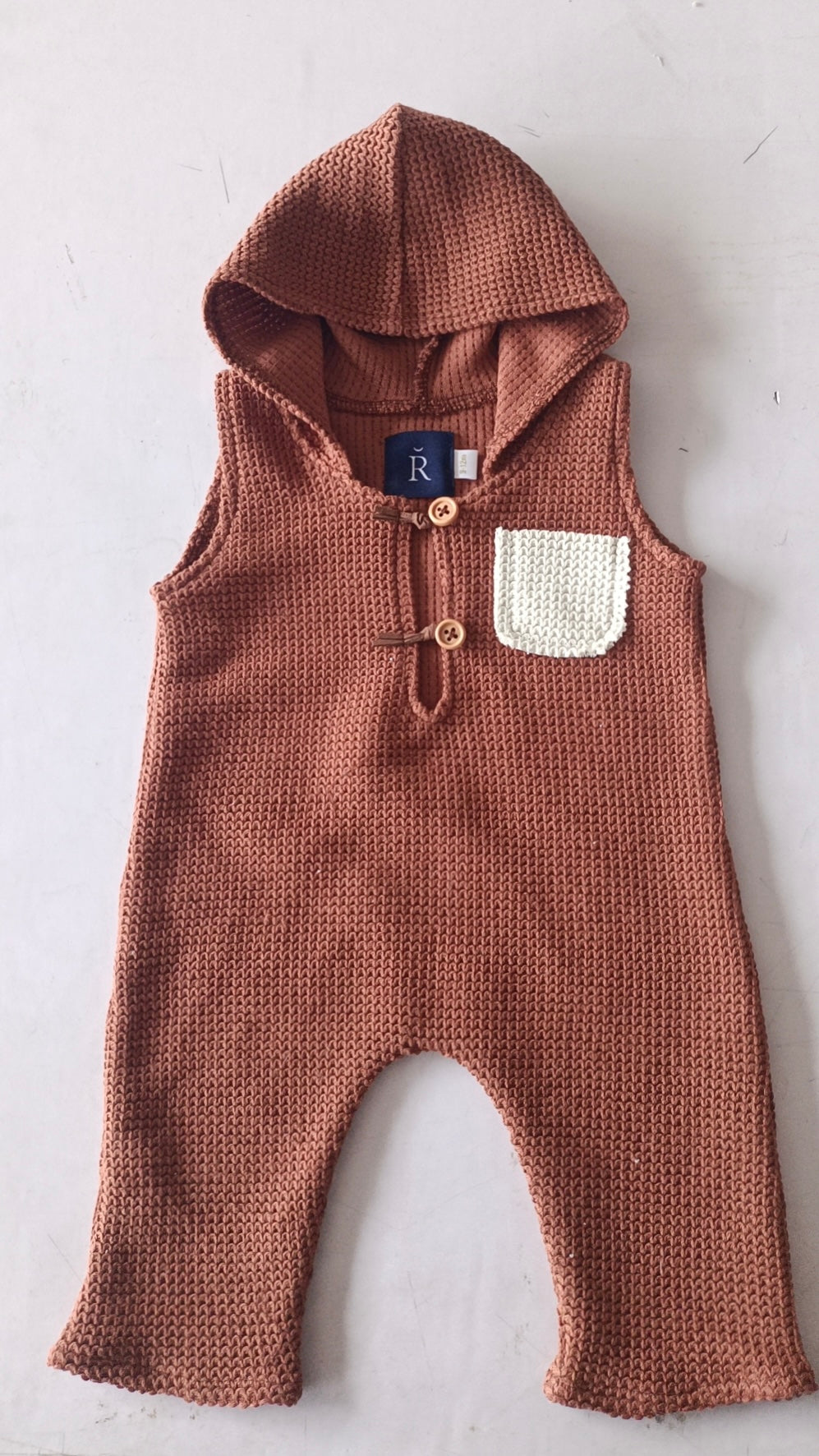 Brown knitted sleeveless hooded sitter romper for photoshoot with white pocket and wooden buttons