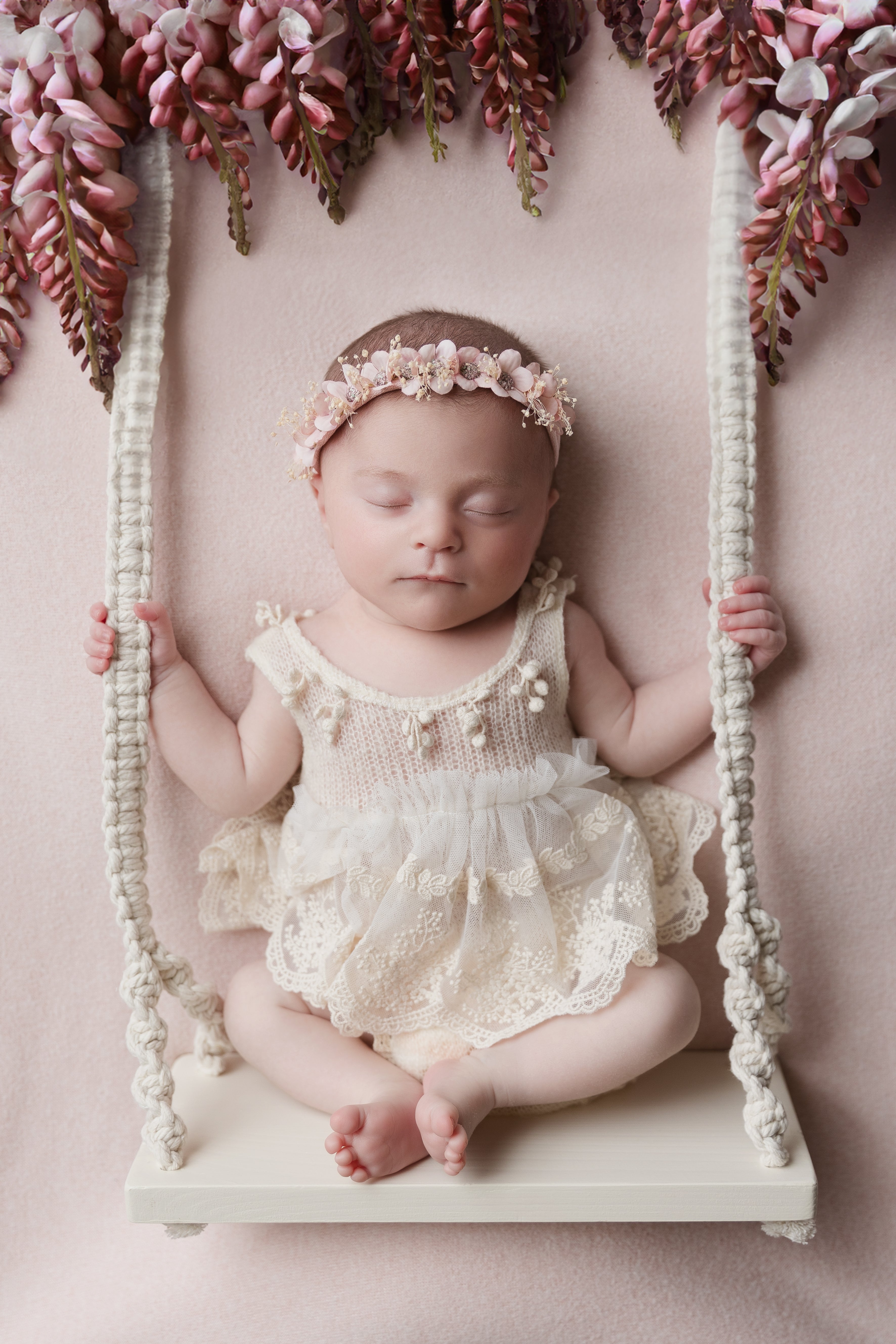 Newborn baby wearing a delicate newborn lace romper outfit and floral headband sitting on a swing