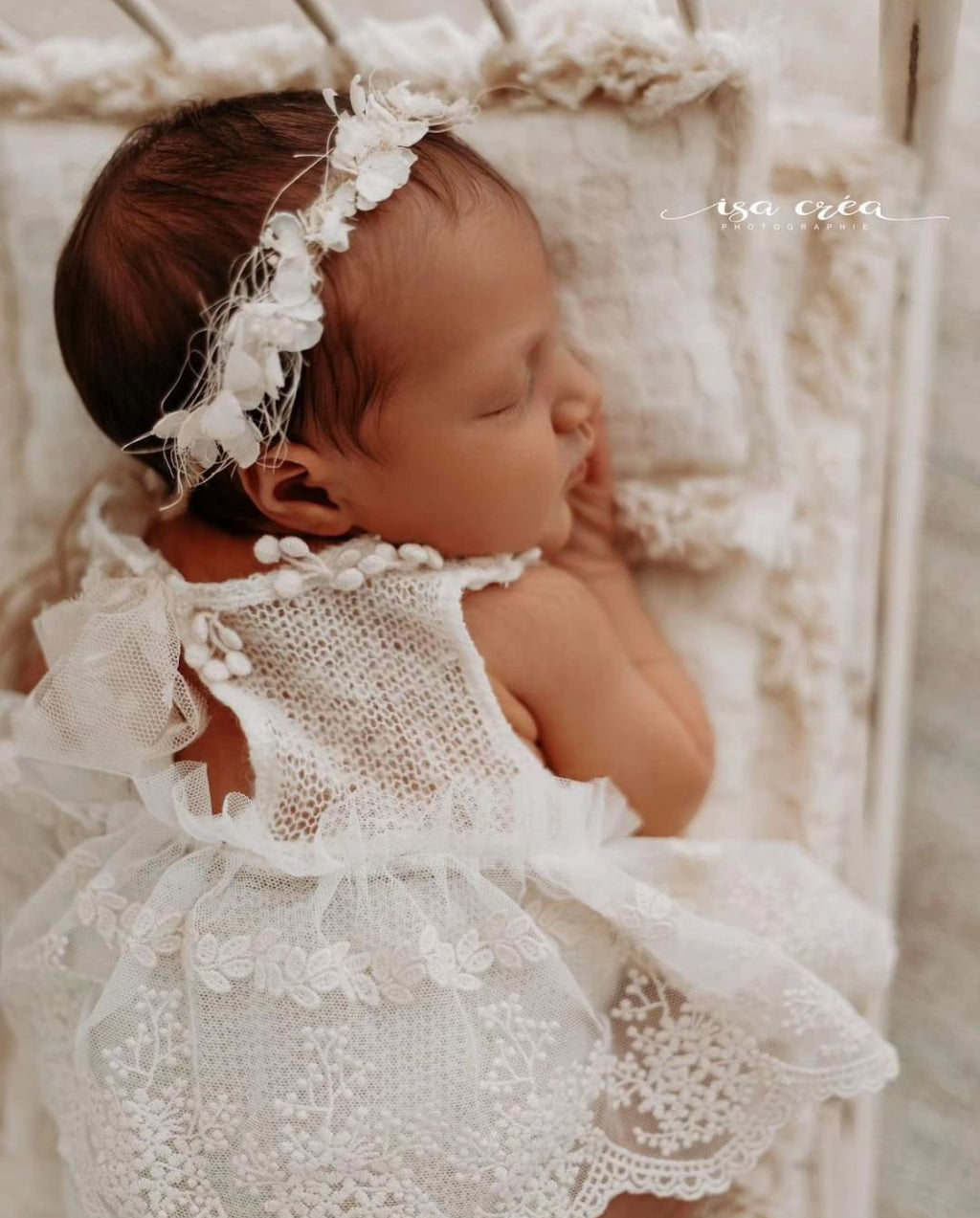 Newborn baby wearing a delicate newborn lace romper outfit with floral headband lying on a soft blanket