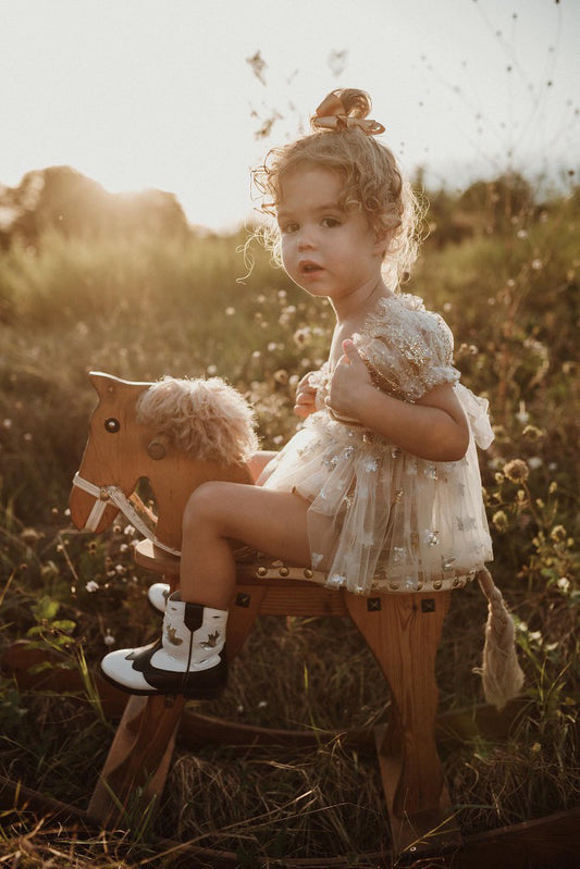 Girls wearing a floral photography prop dress for girls sitting on a wooden rocking horse outdoors